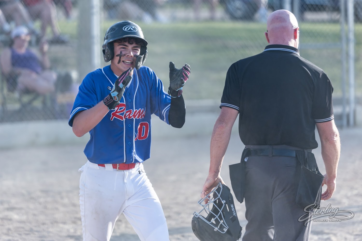 A baseball player in a blue and red uniform celebrates with an umpire nearby on a dirt field.
