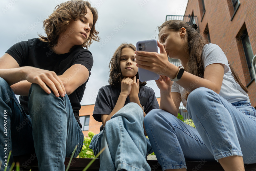 Three young people look at a phone together outdoors.