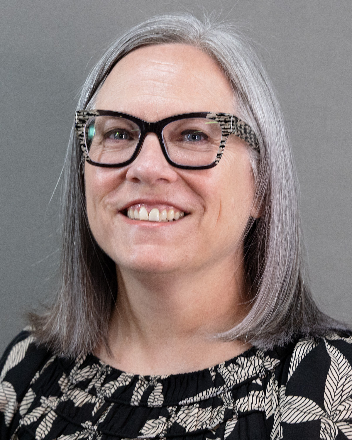 A woman with gray hair and glasses smiles at the camera.