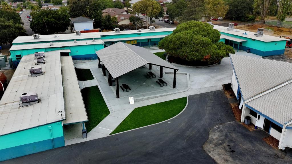 An aerial view of a school campus with buildings, a covered picnic area, and green spaces.