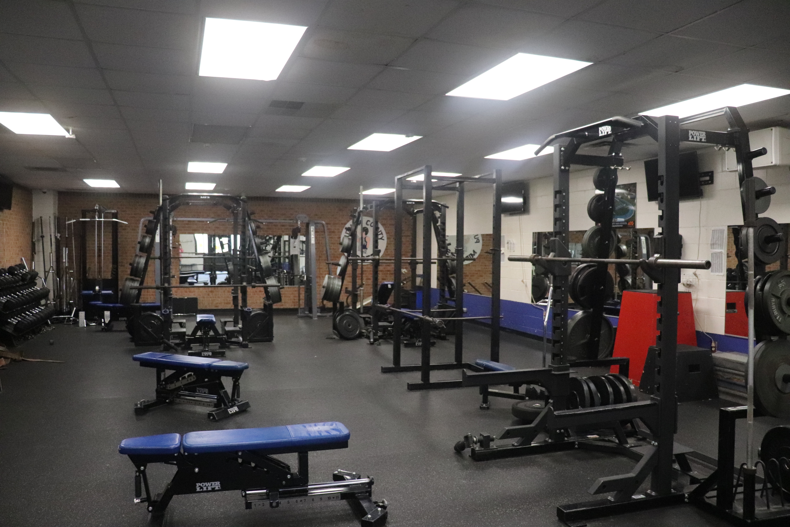 A well-equipped fitness center featuring weight racks, benches, and dumbbells on a rubber floor.