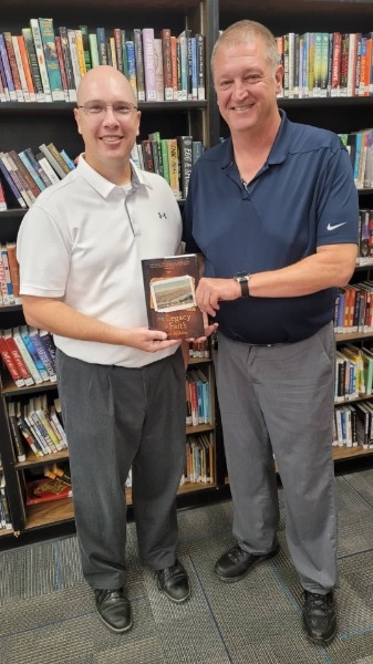 Photo of Brian Spielbauer and an administrator holding a book in a library