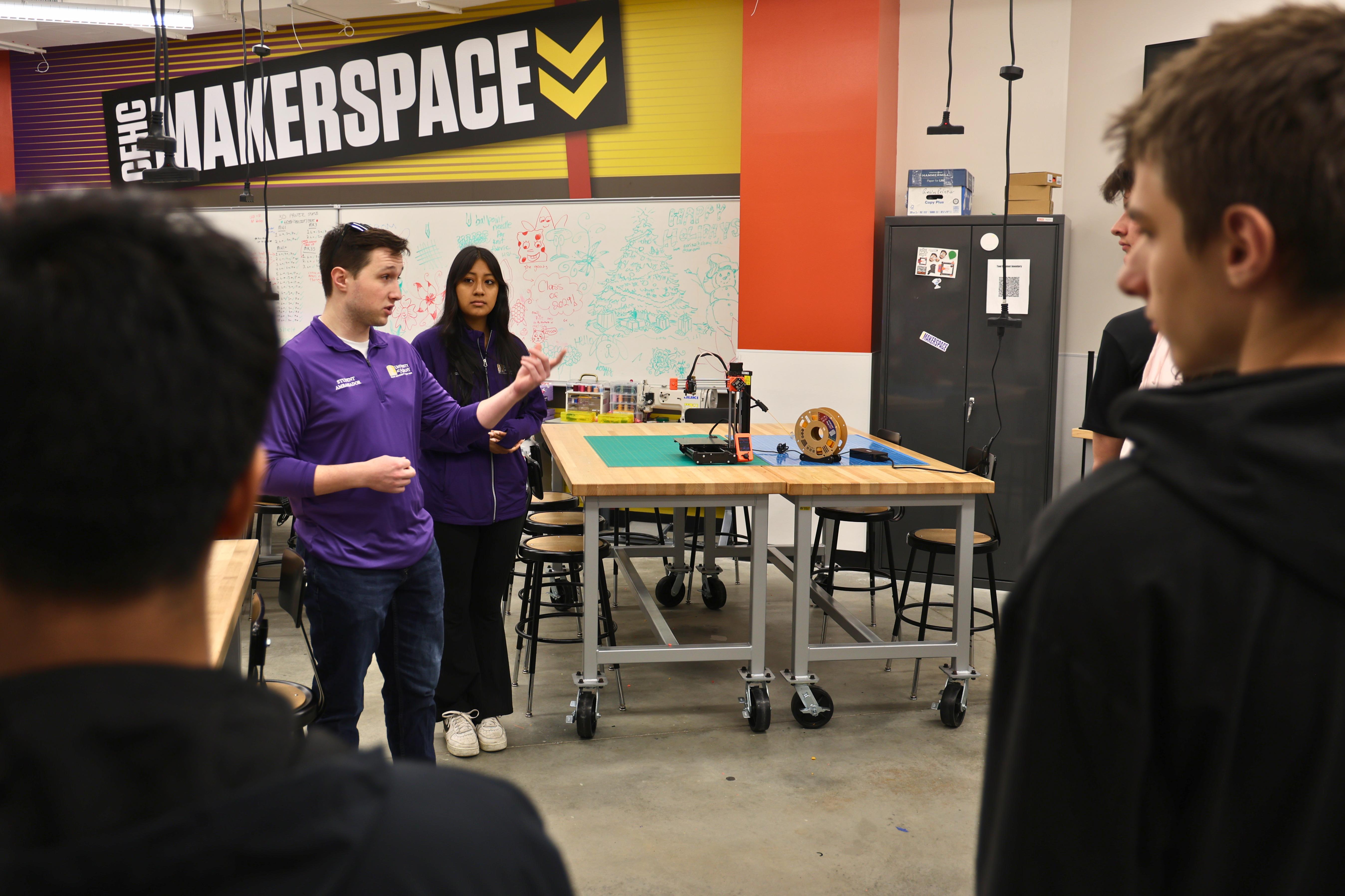 A group of students listens to a speaker in a makerspace.