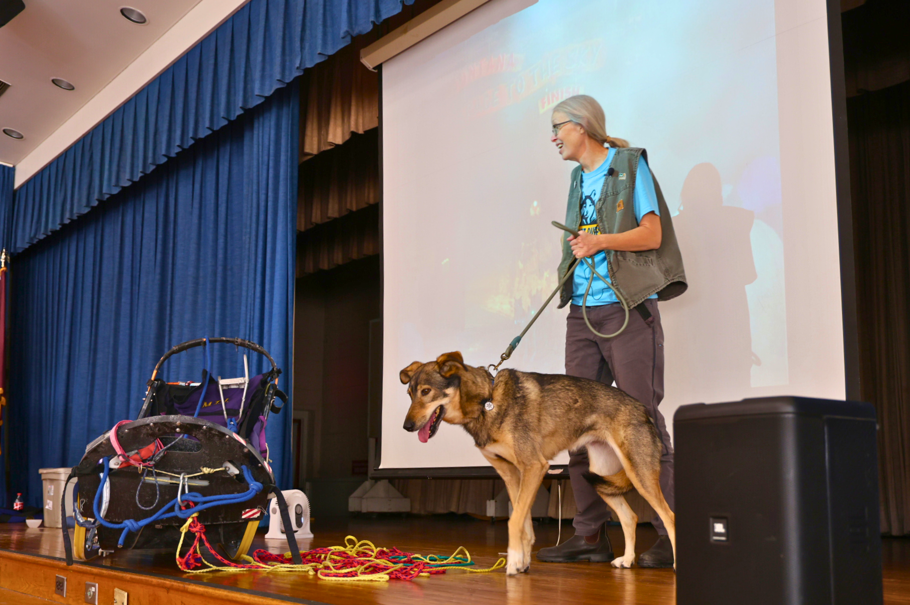 A person stands on a stage with a dog in front of a projection screen.
