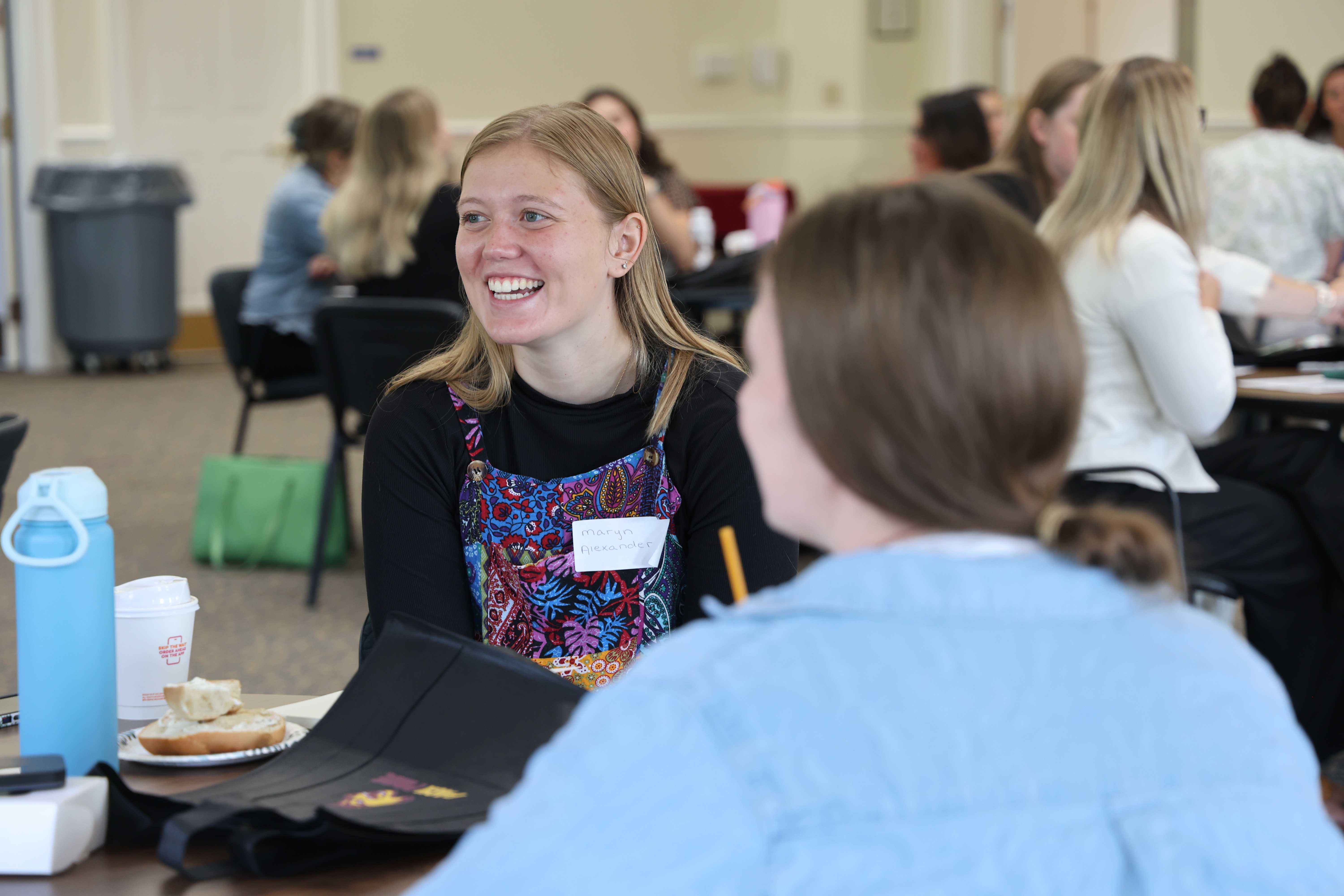 A young woman with blonde hair smiles broadly while attending a gathering.
