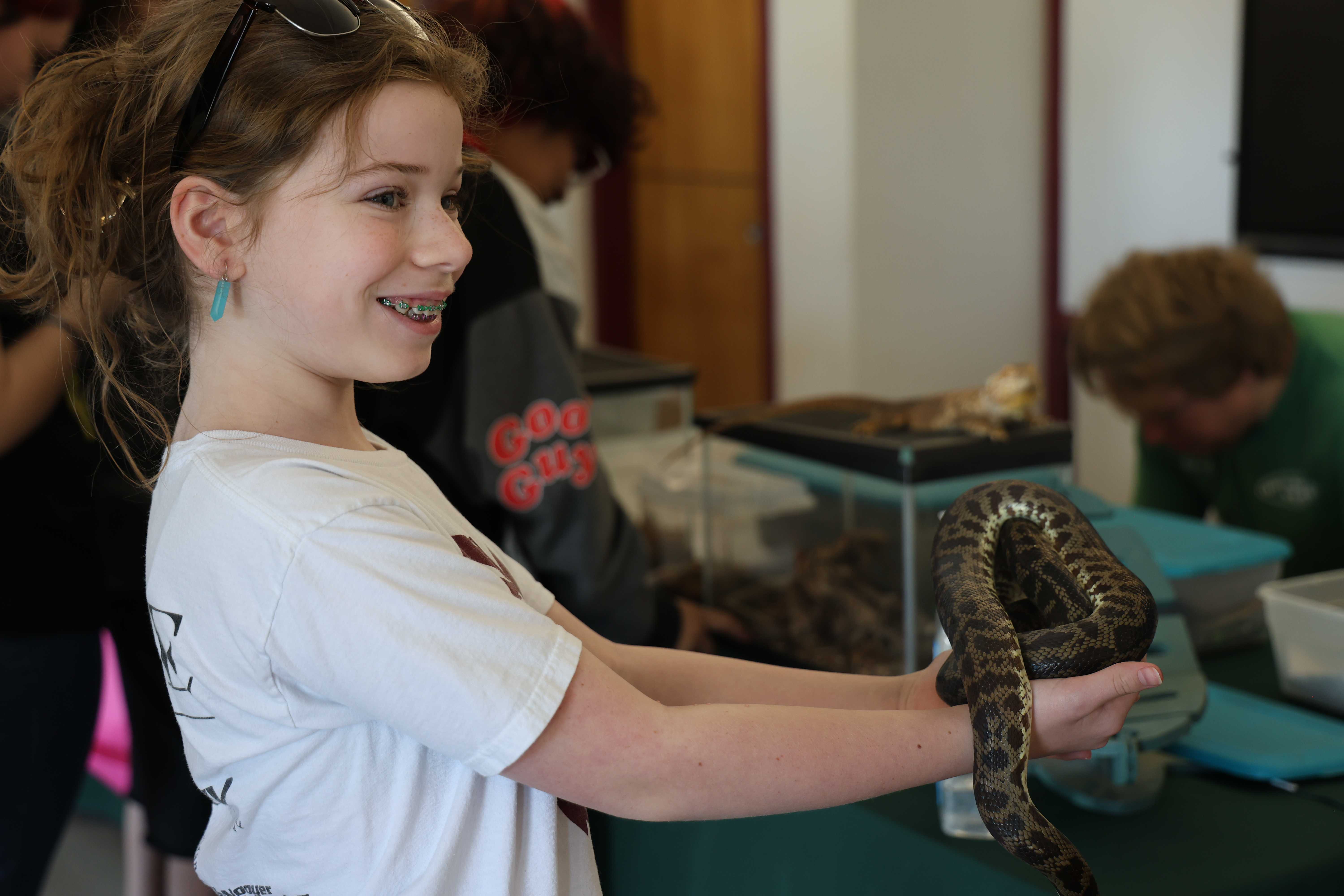 A girl smiles while holding a snake at an event.