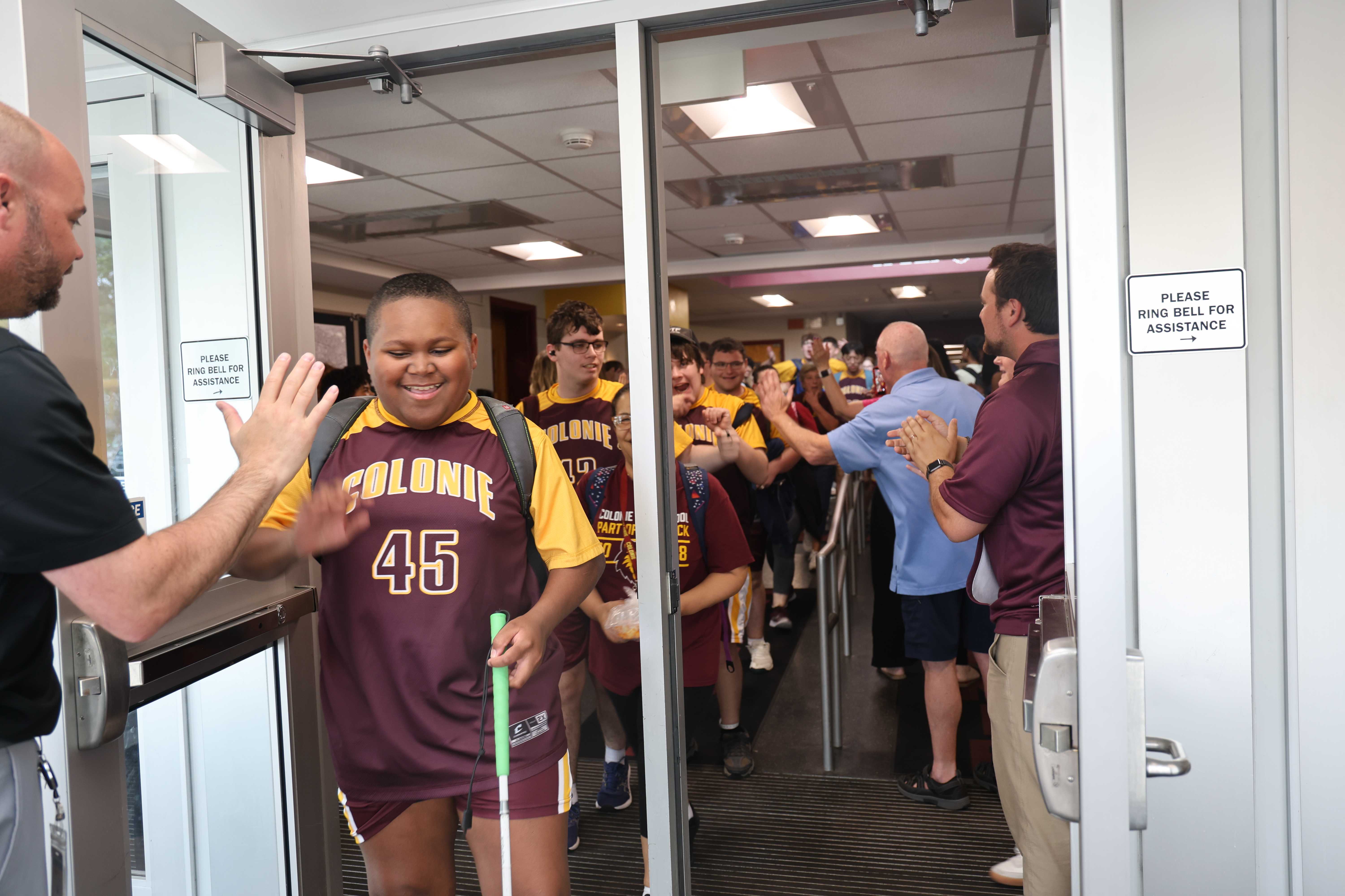 A student in a maroon and gold jersey high-fives someone as they leave a building.