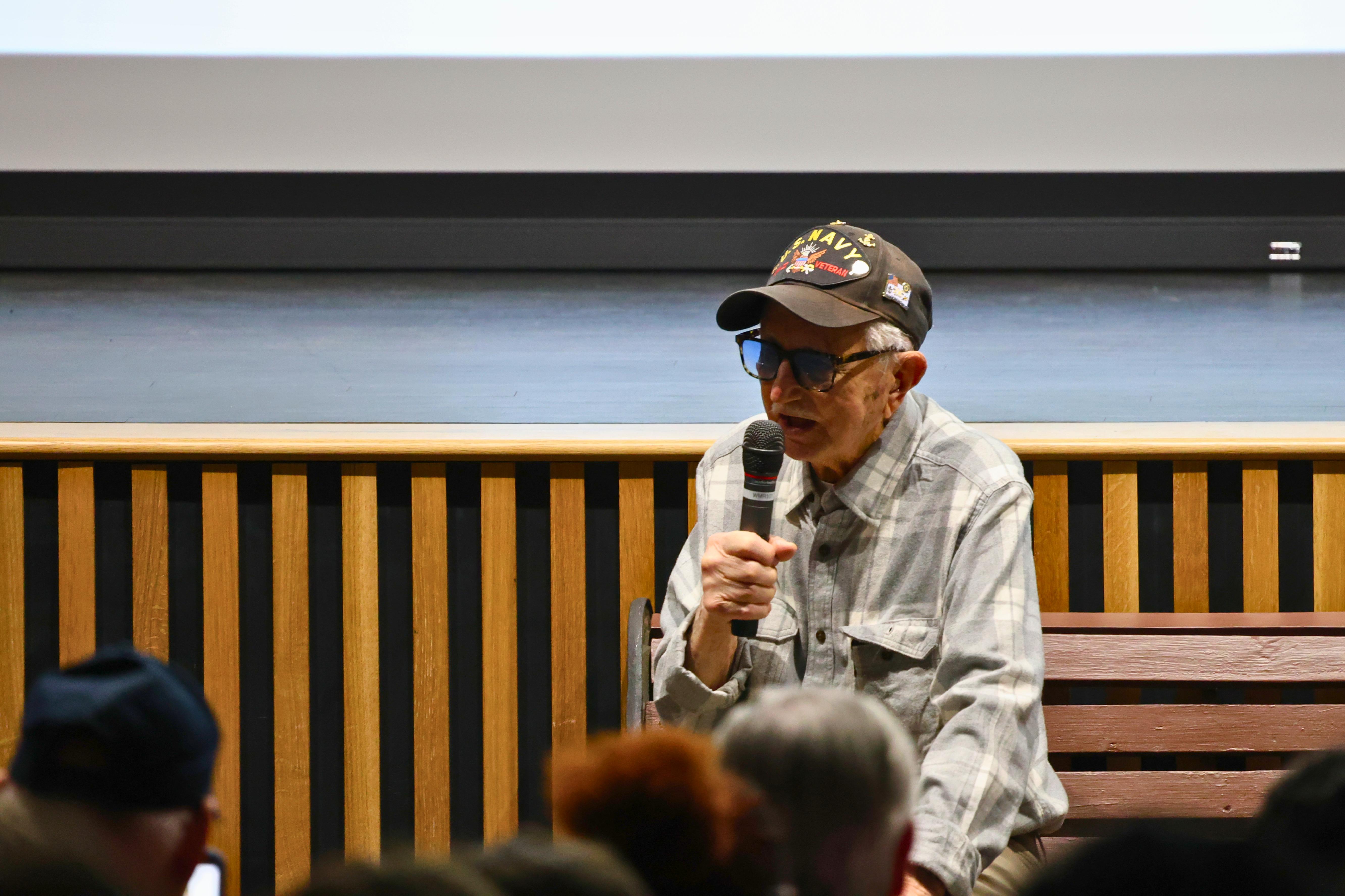 A person speaks into a microphone in front of an audience.