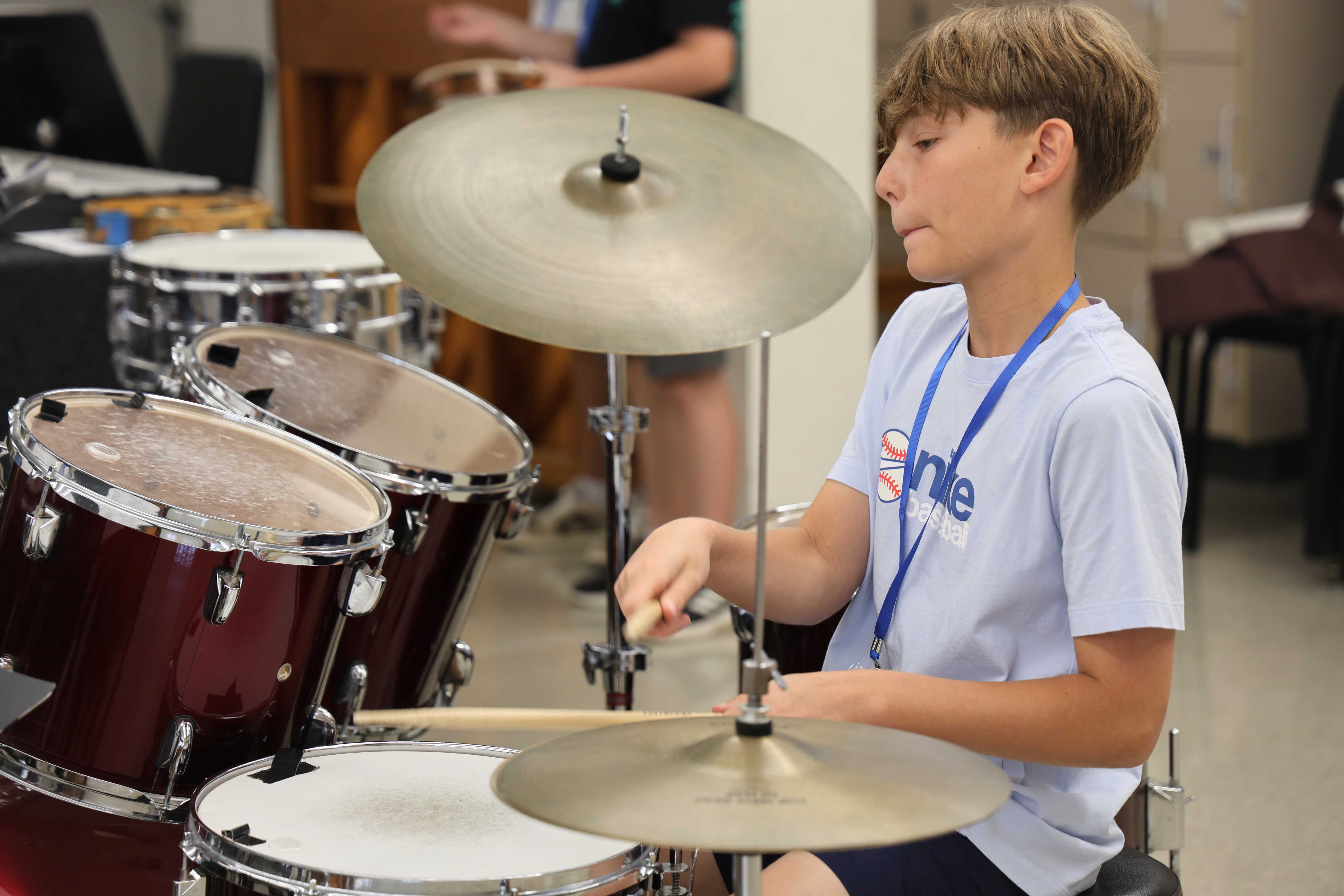 A young boy with brown hair plays a drum set with drumsticks.