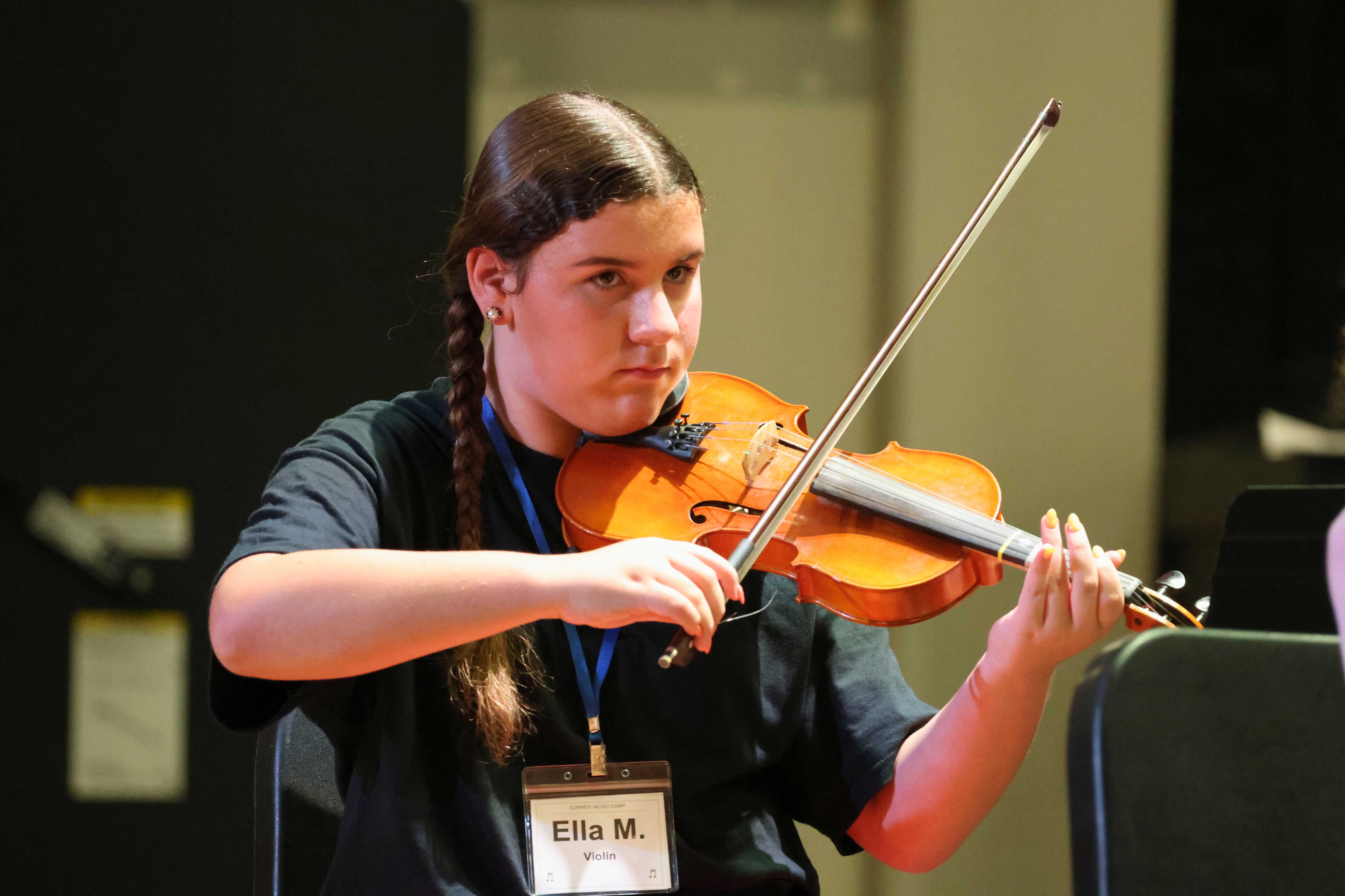 A young person with braided hair plays the violin with a bow, focused on the music.