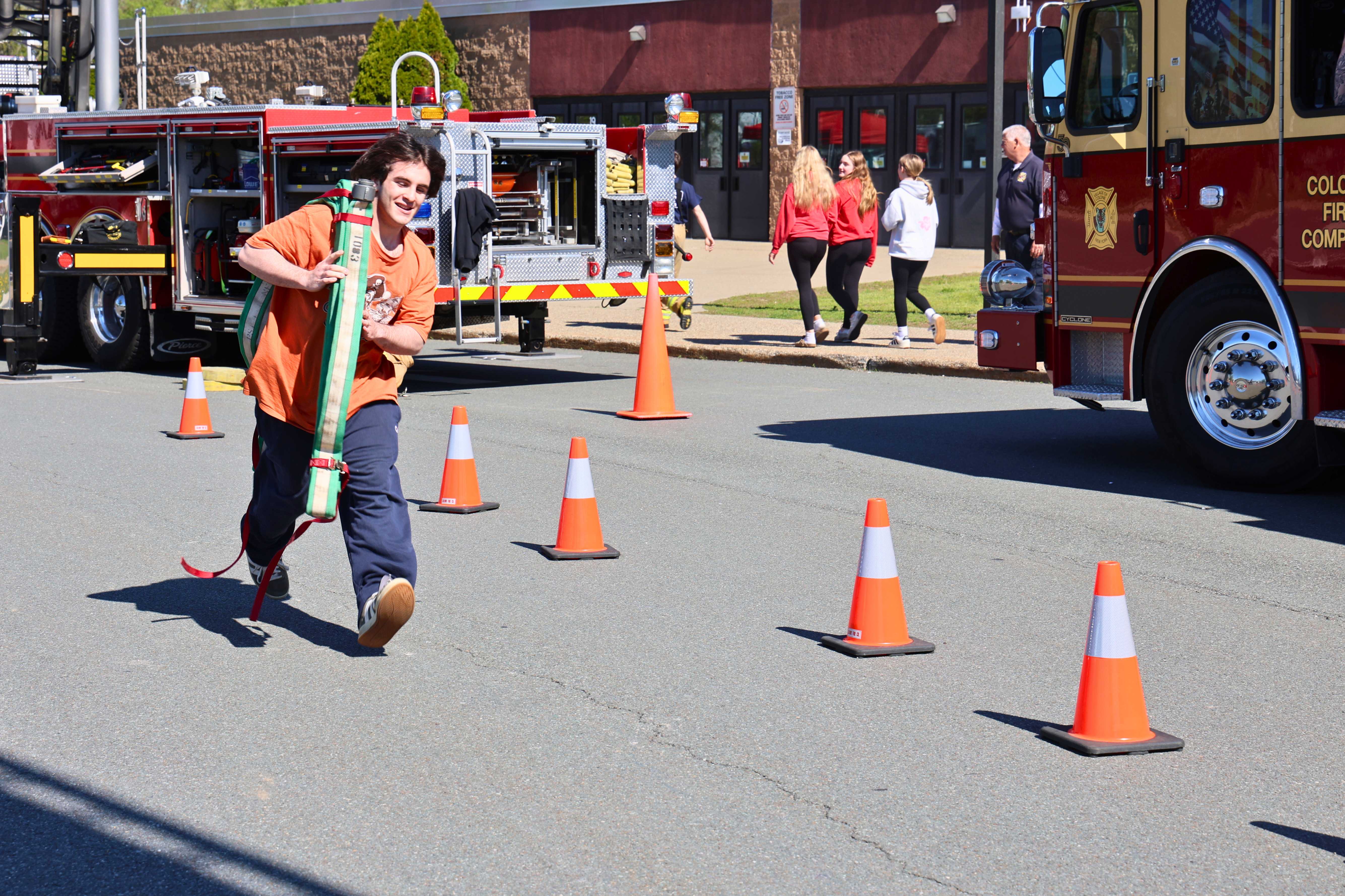 A person runs through an obstacle course with a hose, orange cones mark the path.