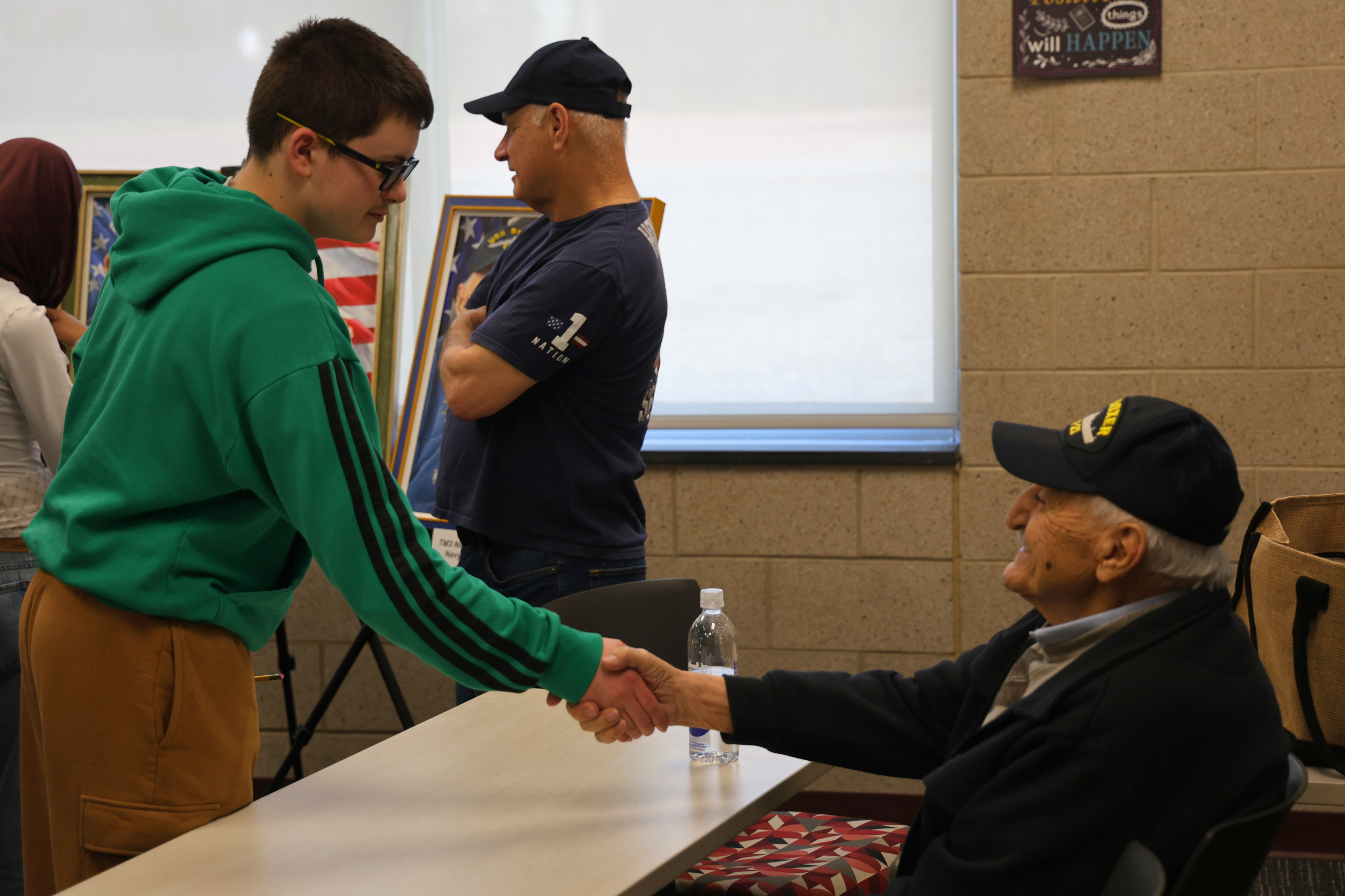 A young man shakes hands with an older gentleman, both smiling.