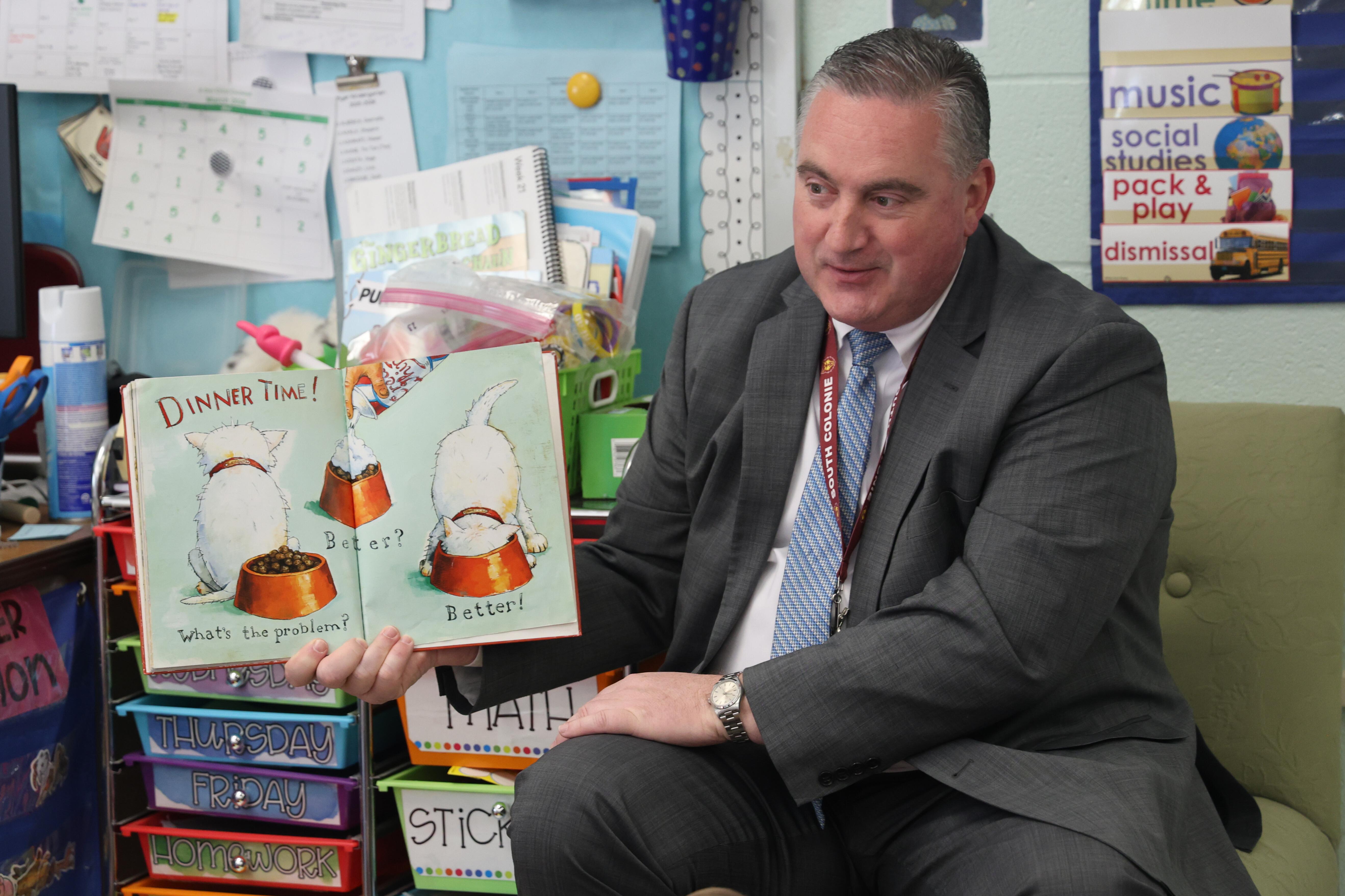 A man in a suit reads a book to a group of children.