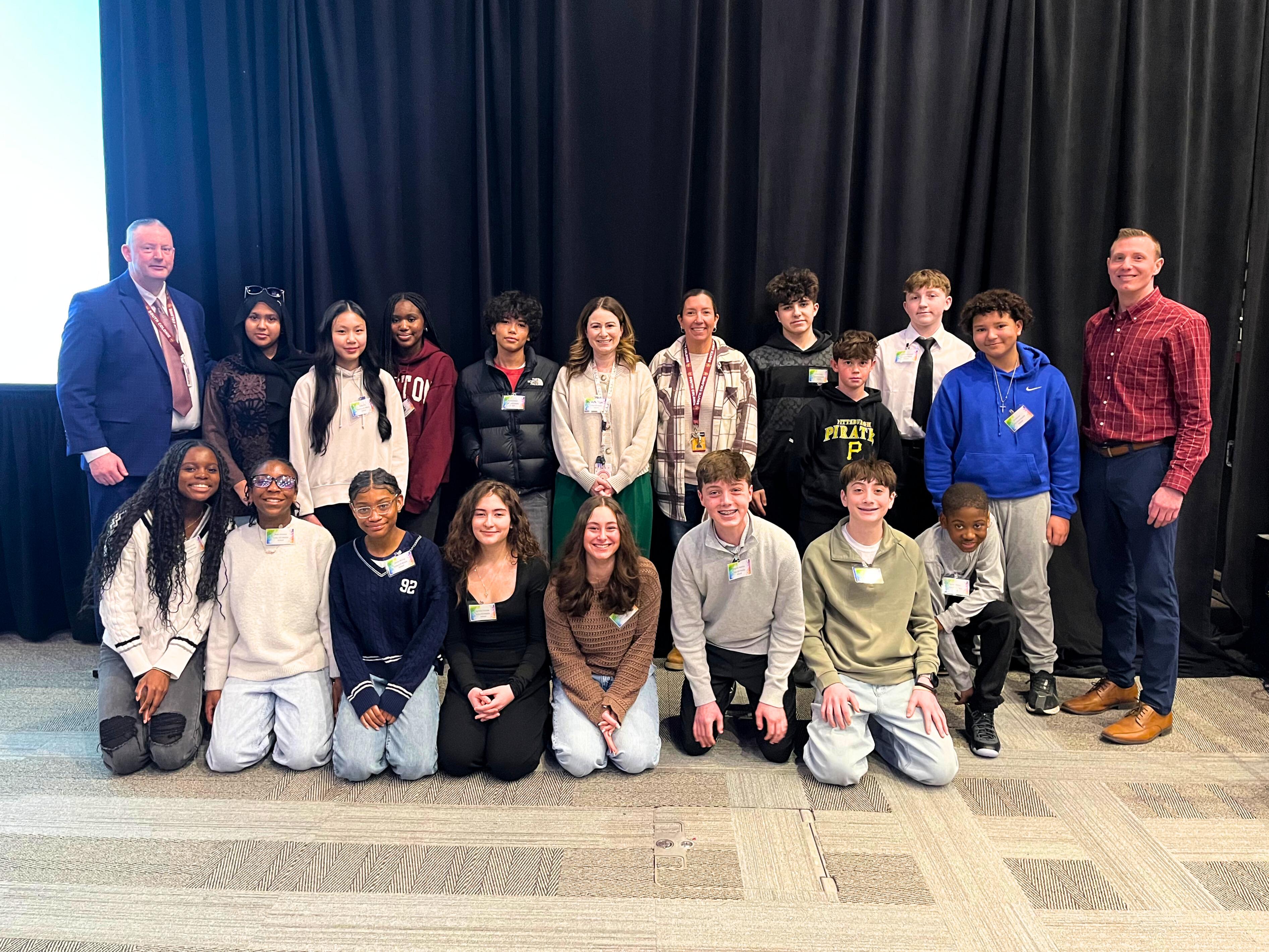 A group of students and adults pose for a photo indoors.