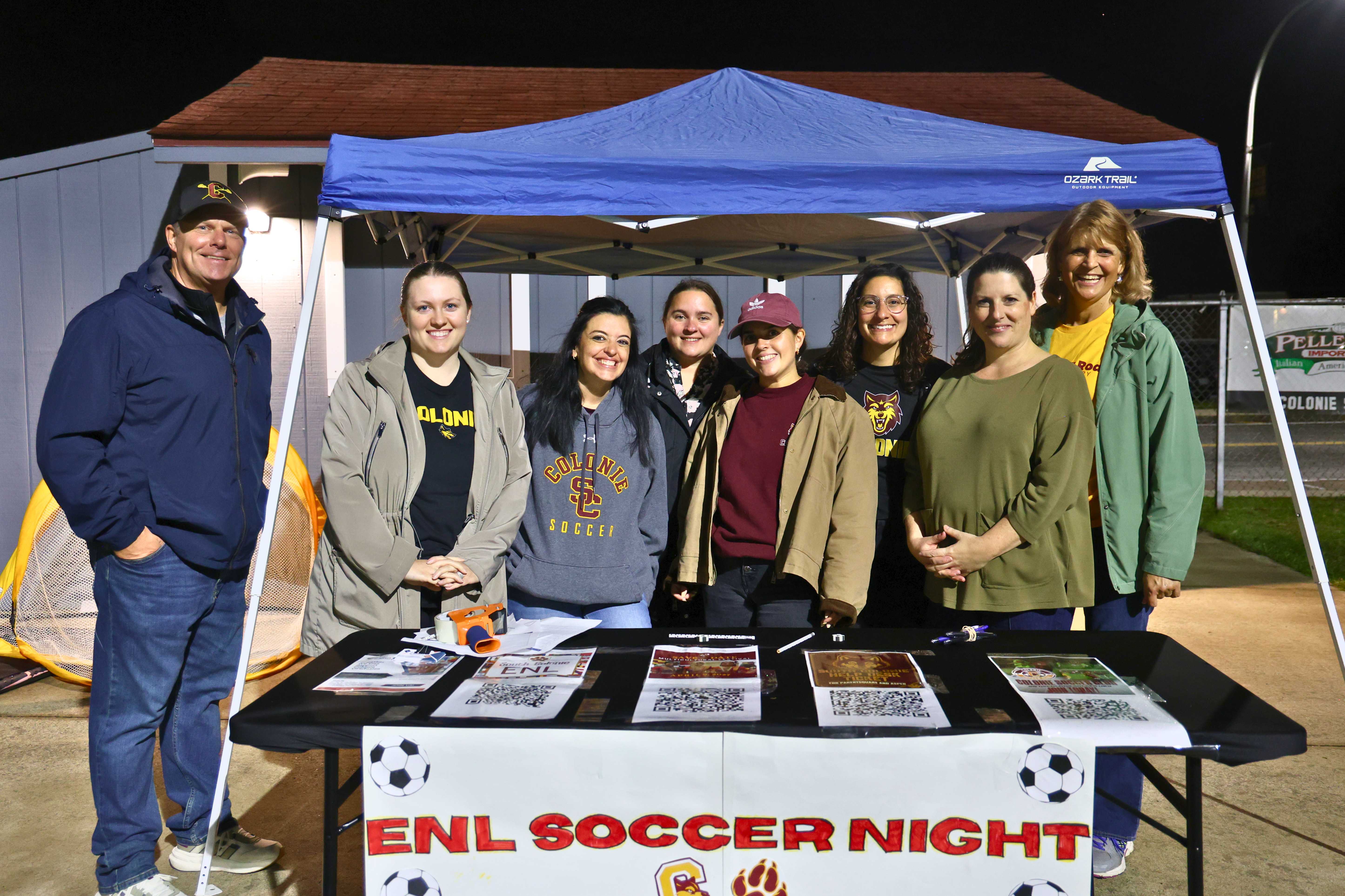 A group of people standing behind a table at an outdoor event called ENL SOCCER NIGHT.
