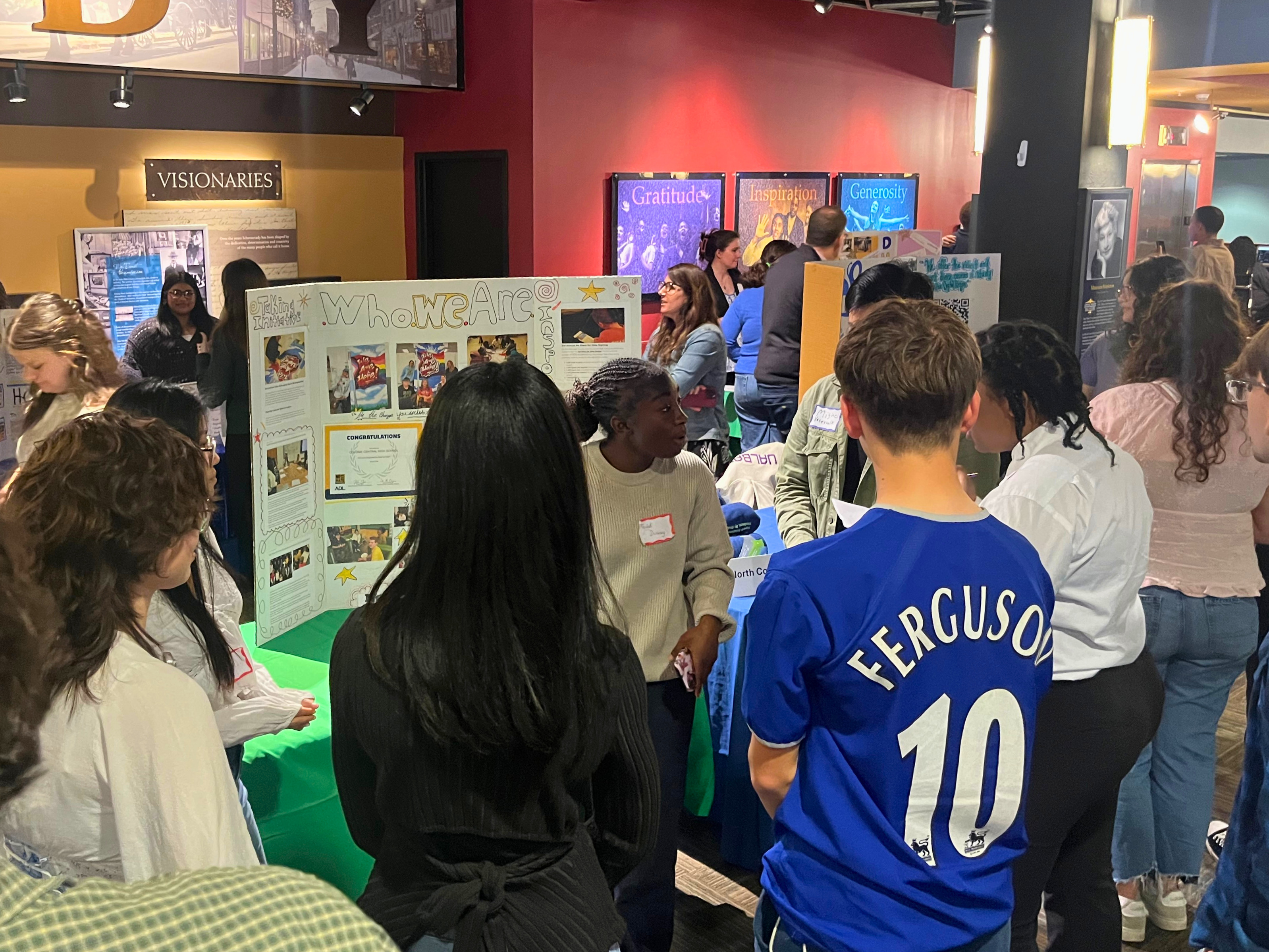 A group of people gather around a display board in a brightly lit room.