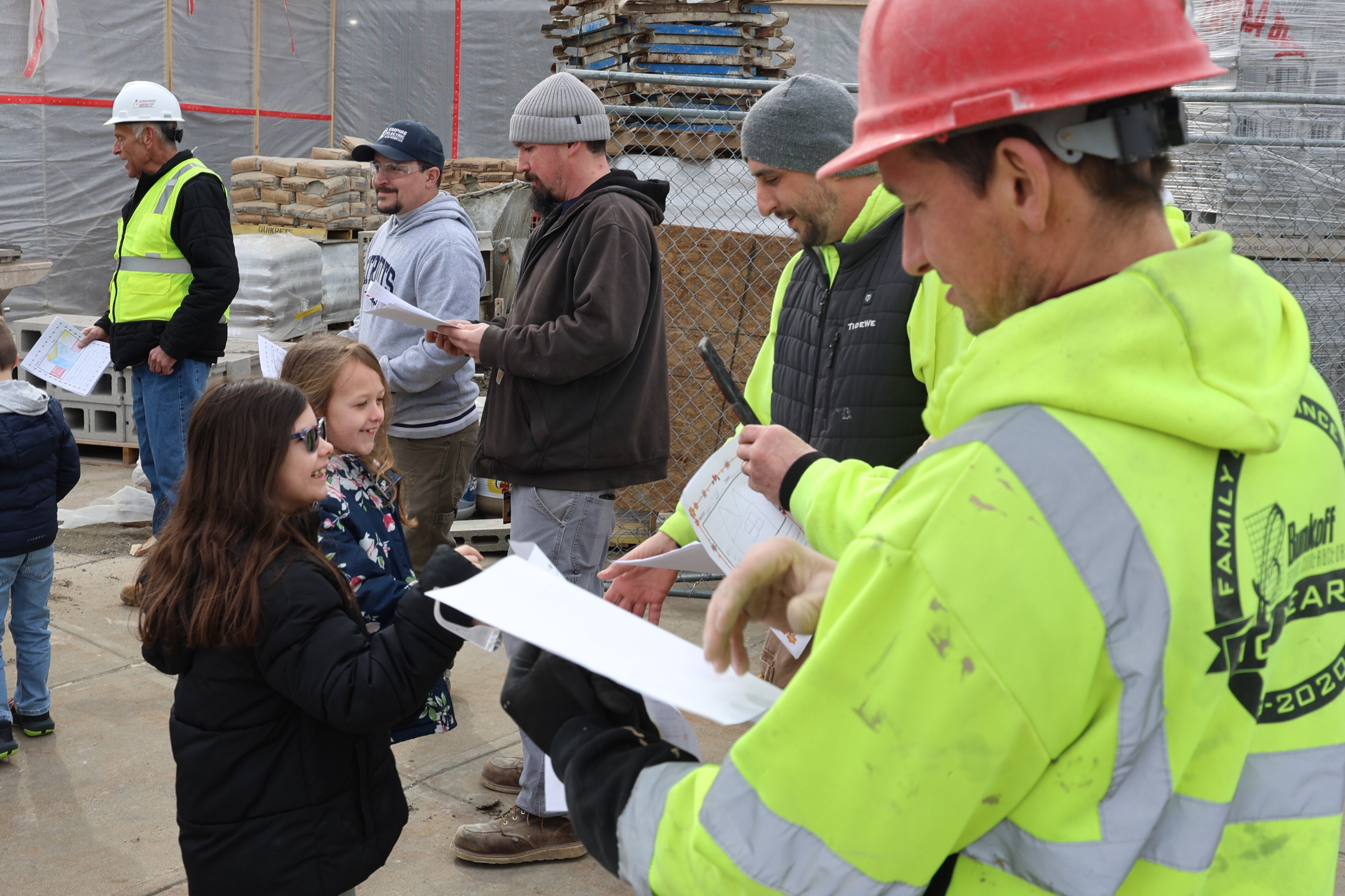 Construction workers interact with children at a building site.