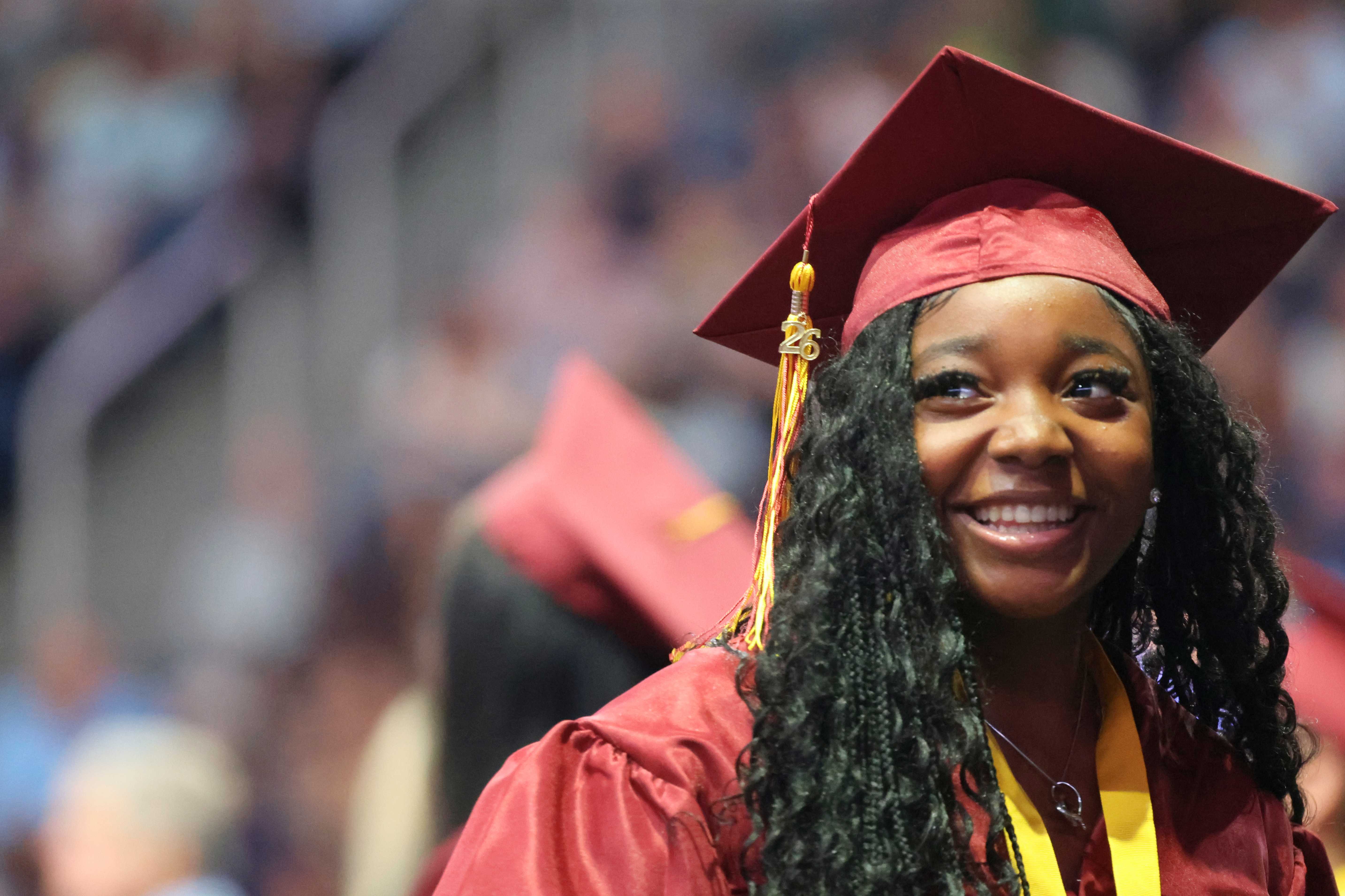 A smiling graduate in a maroon cap and gown looks to the side.