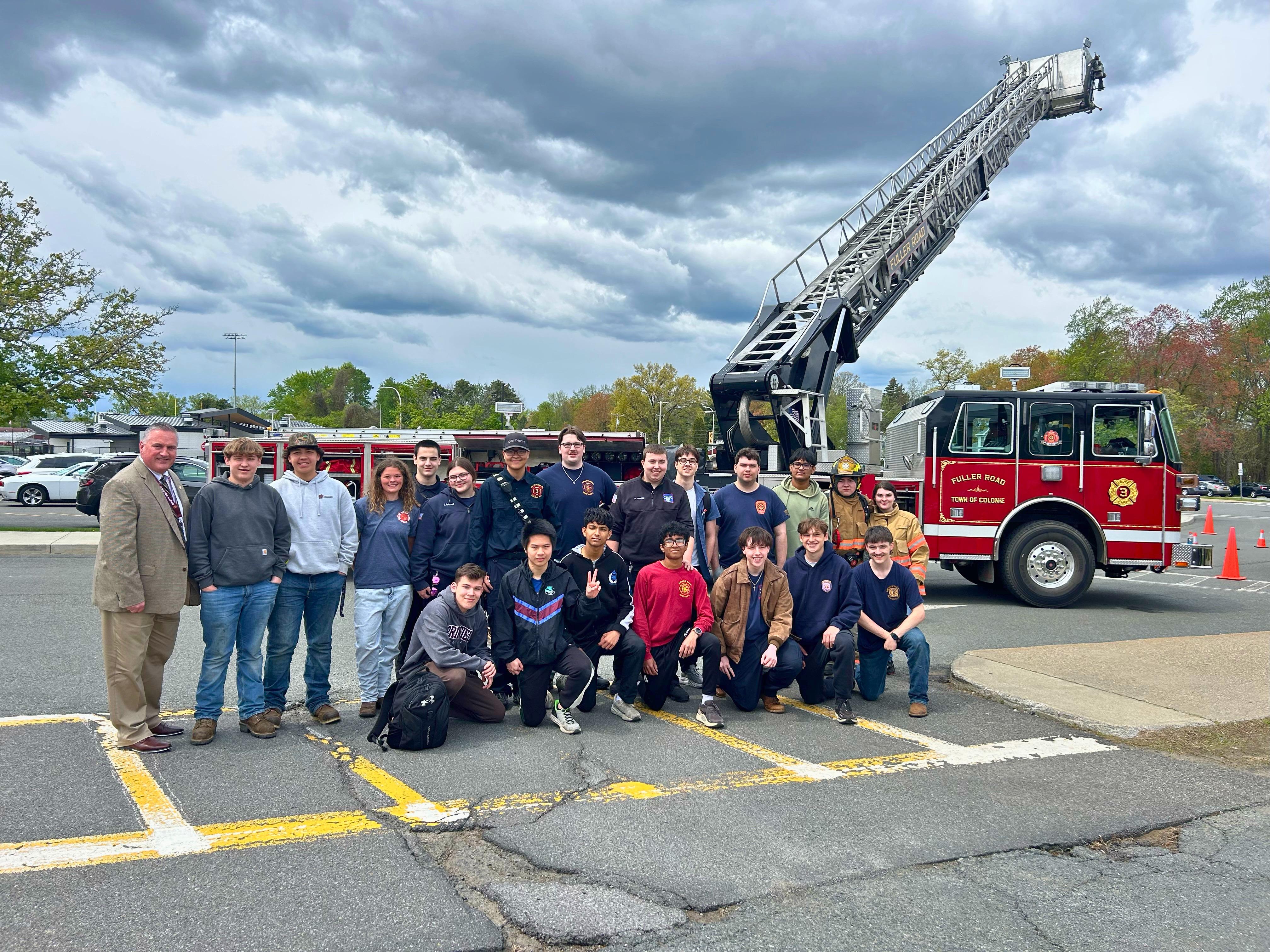 A group of people pose for a photo in front of a fire truck with an extended ladder.