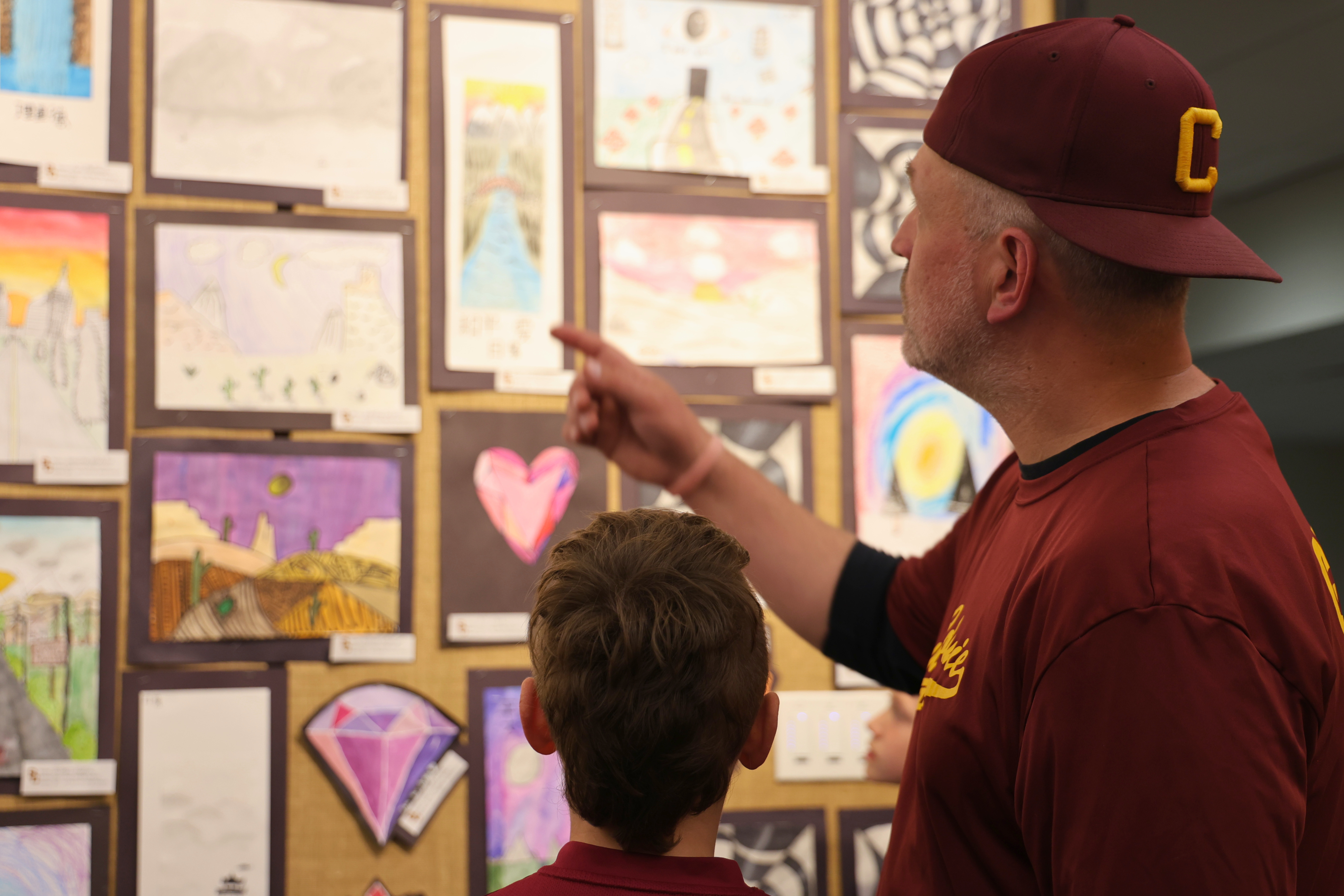 An adult points at artwork displayed on a wall, viewed with a child.
