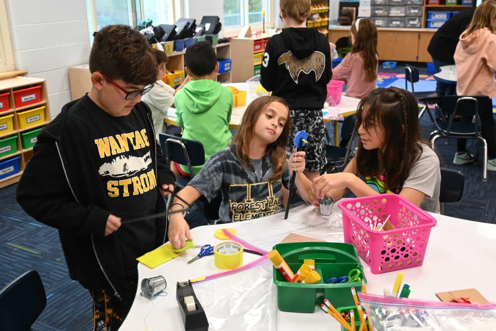 Children work on a craft project at a table in a classroom setting.