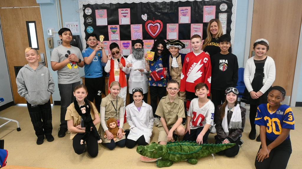 A group of children and a teacher pose for a photo, many in costumes.