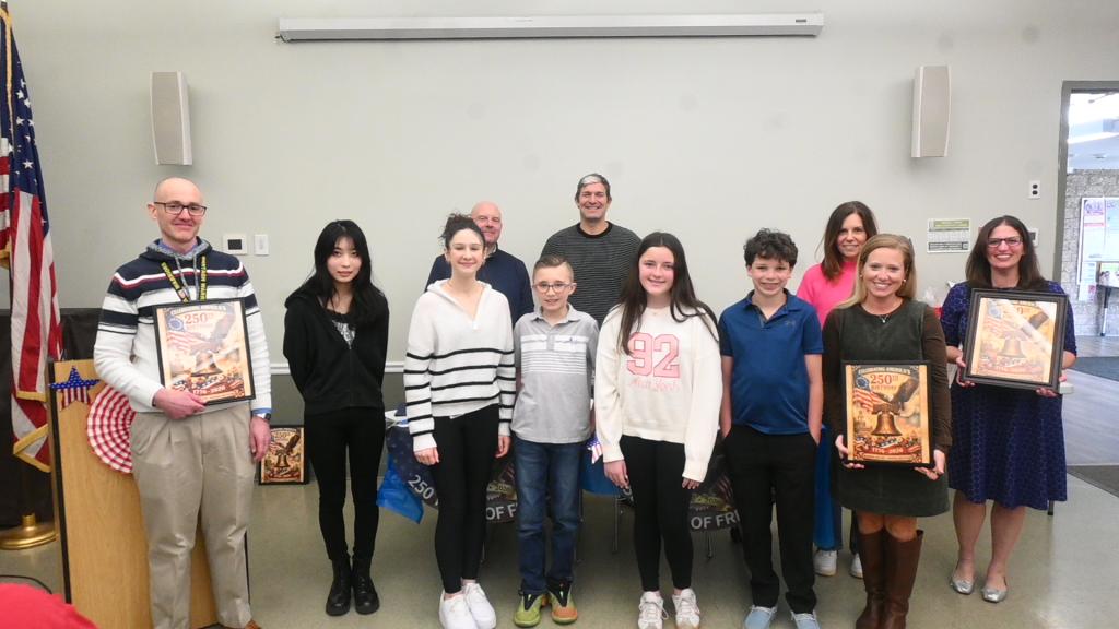 A group of people, including adults and children, pose for a photo indoors, holding framed certificates.