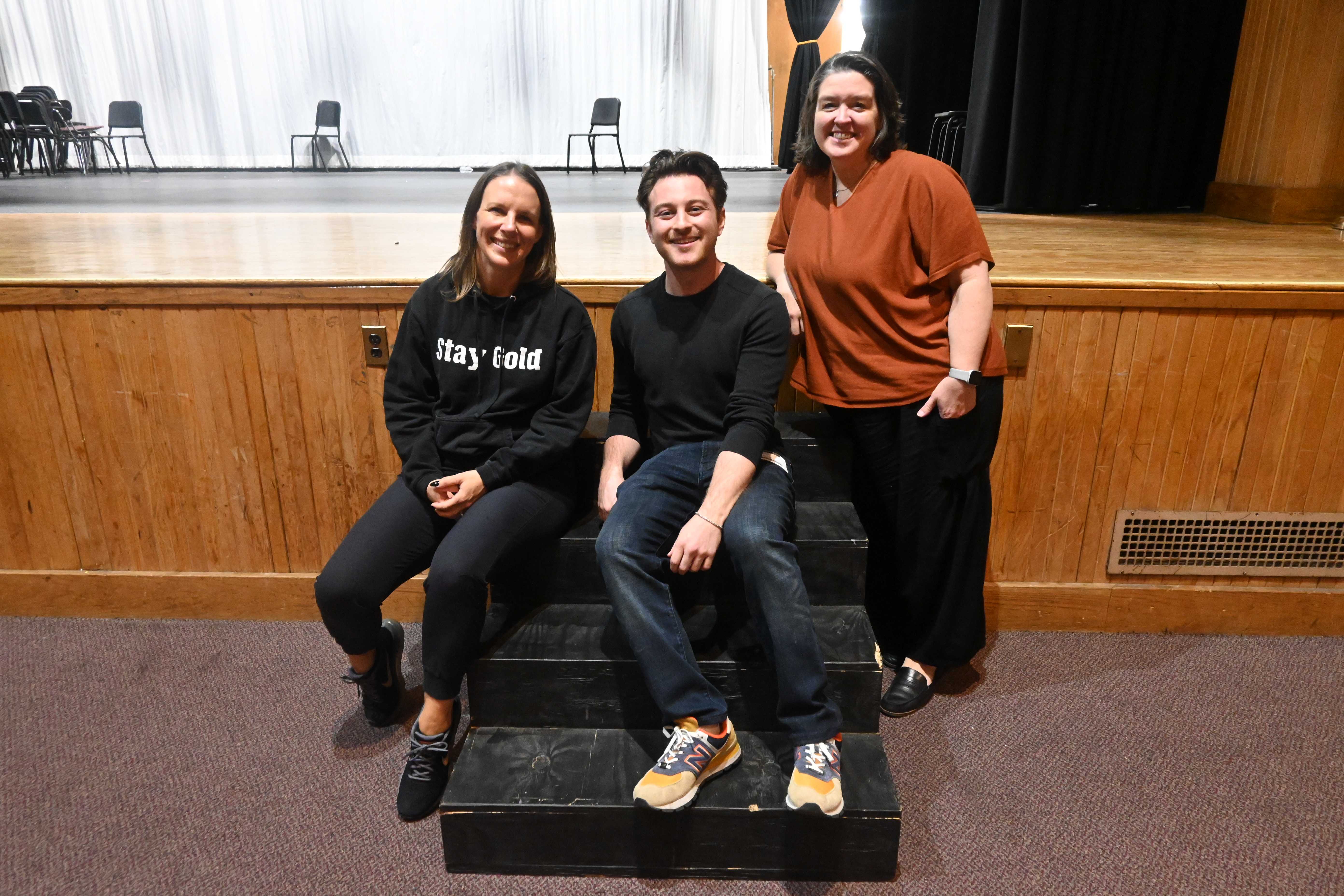 Three people pose for a photo on a small stage, smiling at the camera.