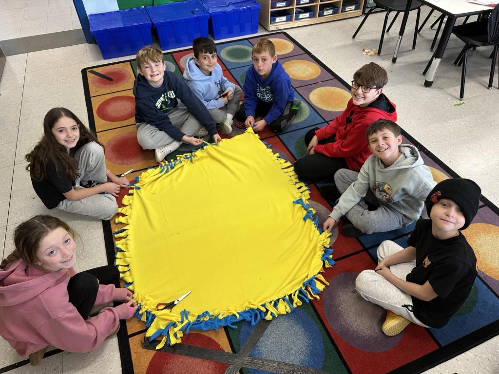A group of children sit in a circle on a colorful rug in a classroom.
