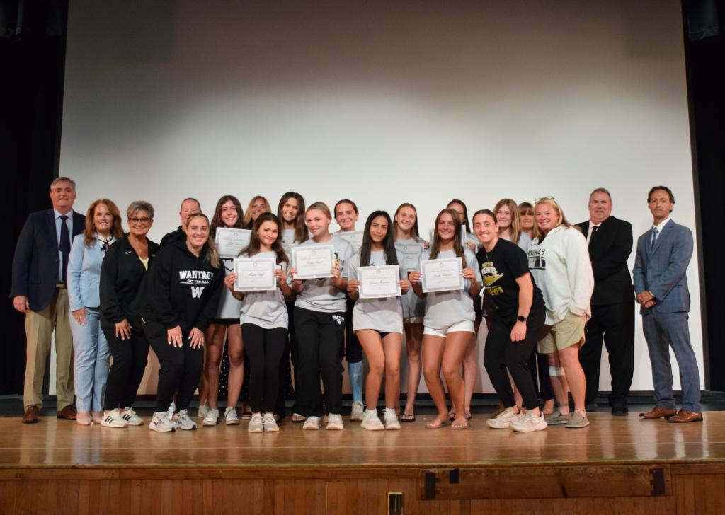 A group of young women and adults stand on a stage, holding certificates.