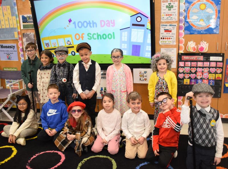A group of children dressed in costumes pose in a classroom.