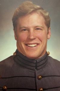 A close-up portrait of a smiling person, Dan Enright, wearing a uniform with a high collar and brass buttons for a posed portrait.