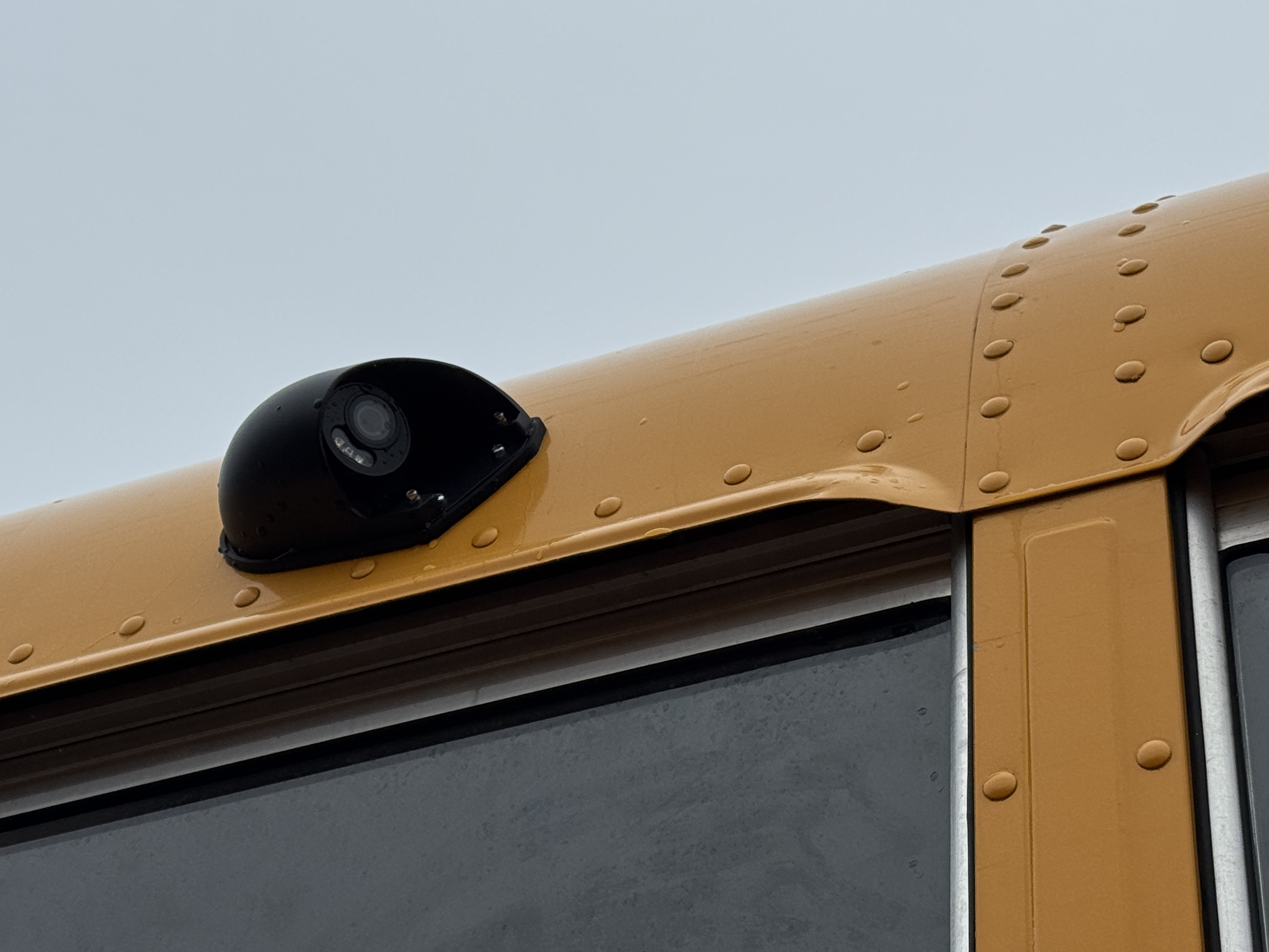 Close-up of a yellow school bus roof with a black camera.