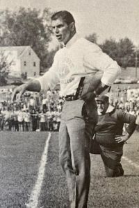 A black and white photo shows a young coach Pete Logan gesturing on a football field sideline.