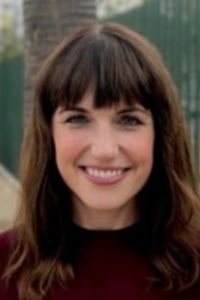 A close-up portrait of a smiling woman, Shannon Smith, with brown hair and bangs, outdoors.