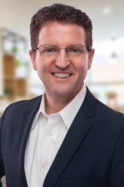 A smiling man in a suit and glasses poses for a professional headshot.