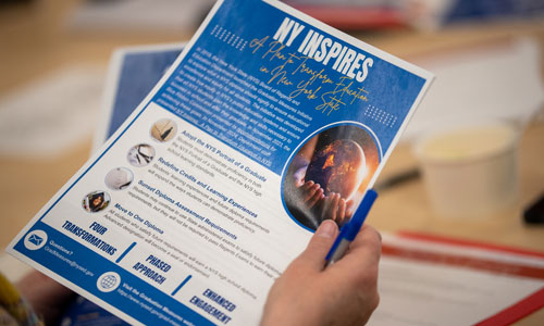An attendee of Coffee & Conversations holds an informational flyer about NY Inspires