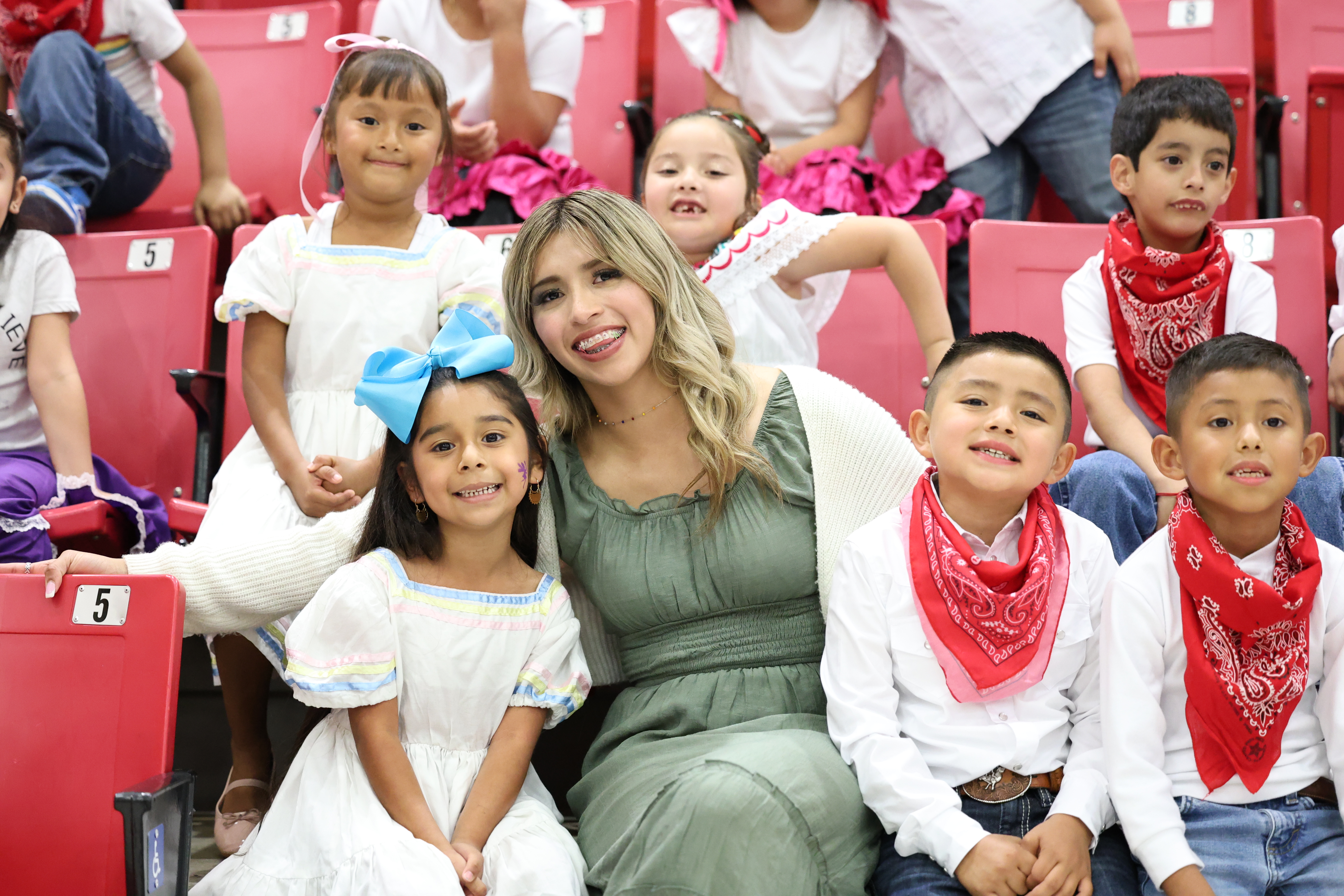 A group of young cheerleaders in red uniforms are performing a routine on a football field.