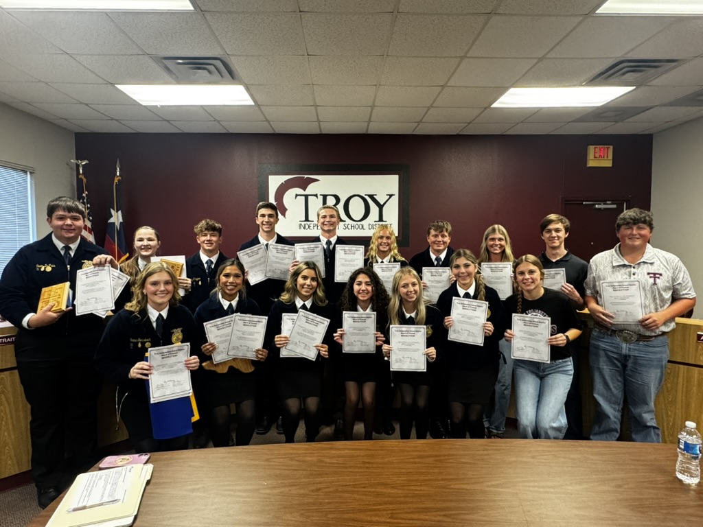 A group of people pose for a photo, holding certificates in a room with a 'TROY' sign.
