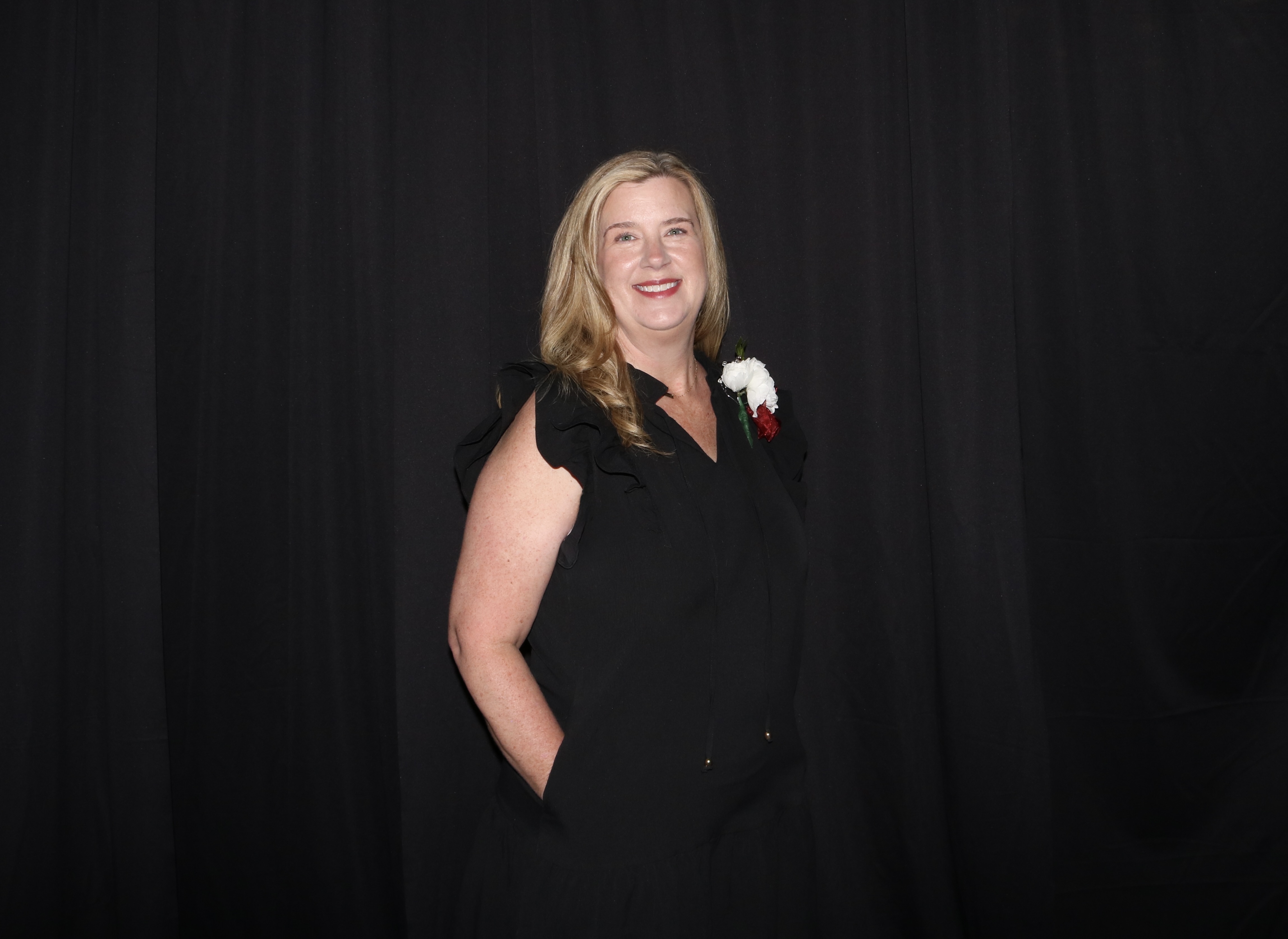 A woman in a black dress smiles against a dark backdrop.