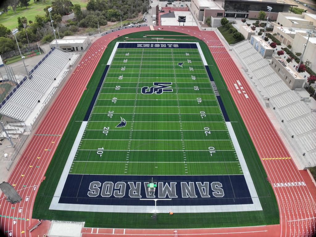 Aerial view of a football stadium with a green field, red track, and bleachers.