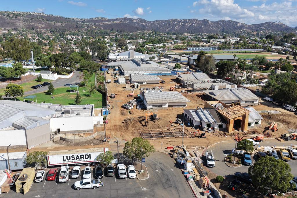 An aerial view of a school campus under construction, featuring multiple buildings, heavy machinery, and parked cars.