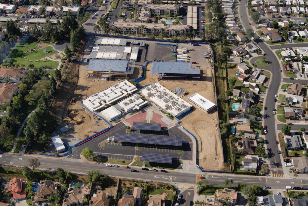 Aerial view of a construction site with buildings, solar panels, and surrounding residential areas.