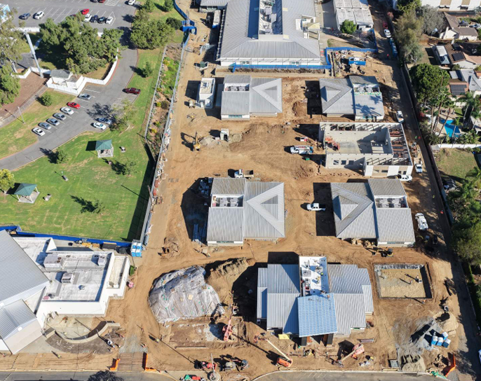 An aerial view shows a new housing development site with several single-story homes under construction.