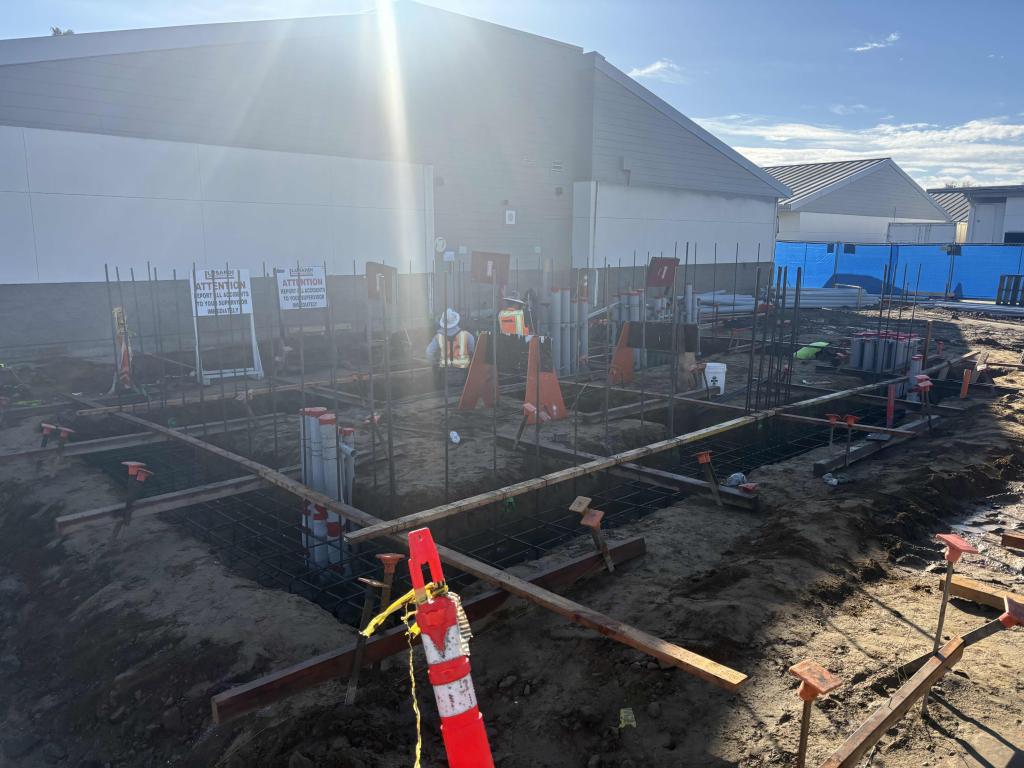 Construction site with exposed foundations and building in the background.