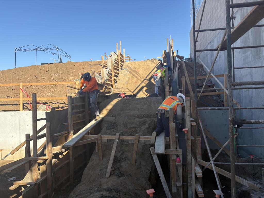 Construction workers build a concrete structure outdoors on a sunny day.