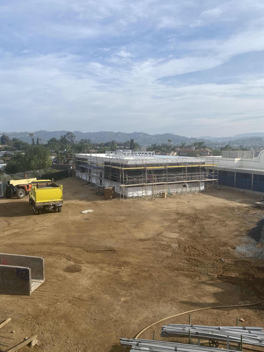 A construction site shows a building in progress with a yellow truck nearby.