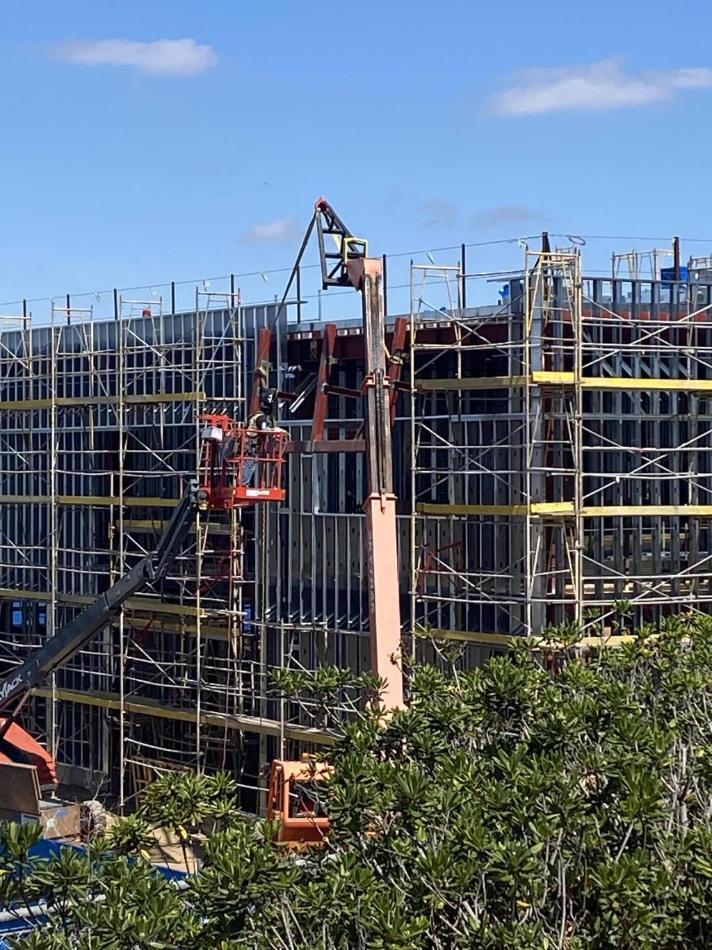 A building under construction with scaffolding and a lift against a blue sky.