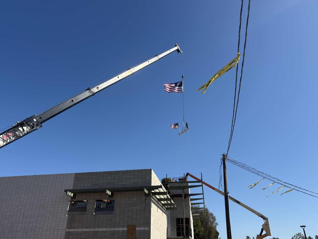 A crane lifts an American flag against a clear blue sky.