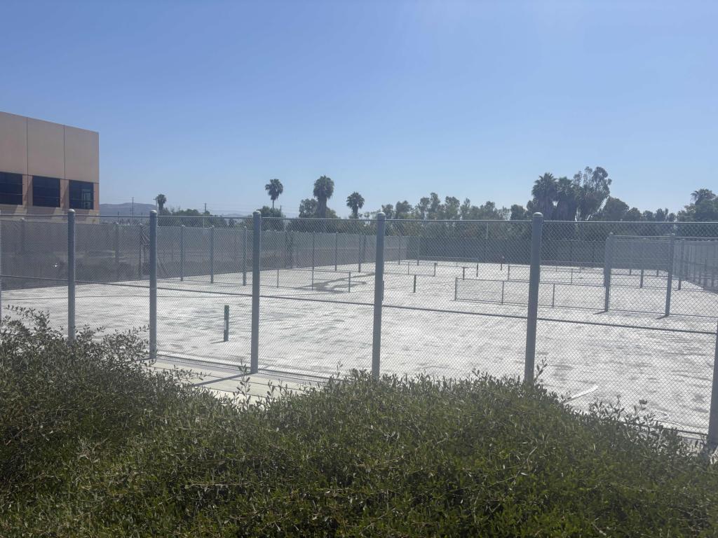 An empty outdoor court with a chain-link fence and a building in the background.